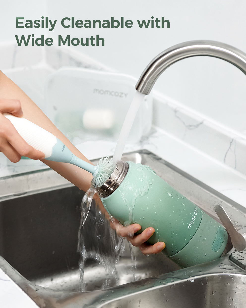 Momcozy portable breast milk warmer, mint green, being cleaned under a faucet. Features wide mouth design for easy cleaning.