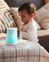 Baby engaged with glowing smart baby sound machine emitting musical notes on plaid-covered table