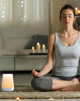 Woman meditating with Momcozy Smart Baby Sound Machine, promoting relaxation and sleep with warm gradient light.