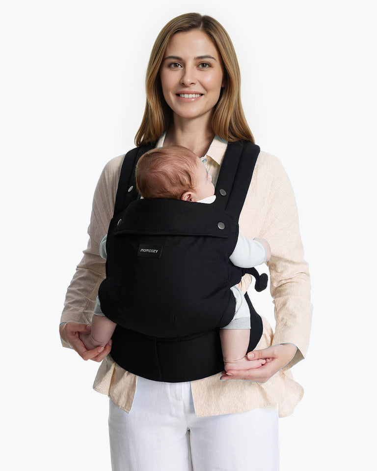 Translation missing: de.Momcozy PureHug Baby Carrier. Black carrier, comfortable design, worn by mother holding baby. Ideal for babywearing